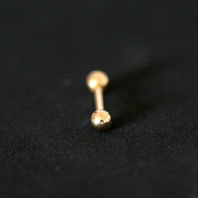 piercing de aço cirúrgico banhado a ouro com haste reta e esferas nas extremidades sobre fundo preto. há uma pedra de cristal em uma das esferas.