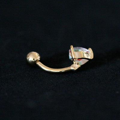 piercing de umbigo da tal da realeza visto por trás em um fundo preto aveludado. a peça é dourada e conta com uma pedra de zircônia em formato de coração.