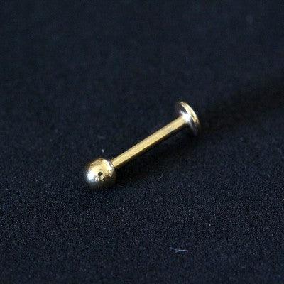 piercing labret da tal da realeza em um fundo preto aveludado. a peça é dourada e possui uma esfera com na extremidade.