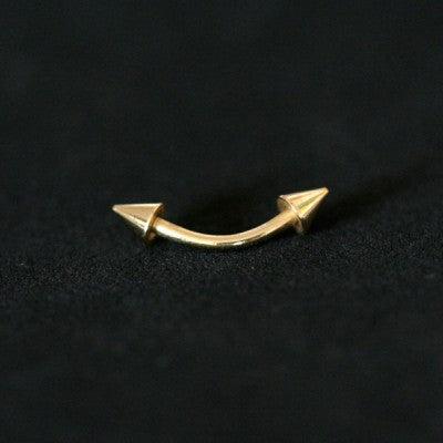 Piercing de aço cirúrgico banhado a ouro com haste curva e spikes nas extremidades sobre fundo preto