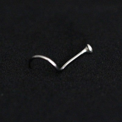 Piercing Nostril em aço cirúrgico da Tal da Realeza em um fundo preto aveludado. A peça tem uma pedra cravada na ponta.