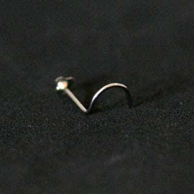 Piercing Nostril em aço cirúrgico da Tal da Realeza em um fundo preto aveludado. A peça tem formato de coração na ponta, com uma pedra de cristal.