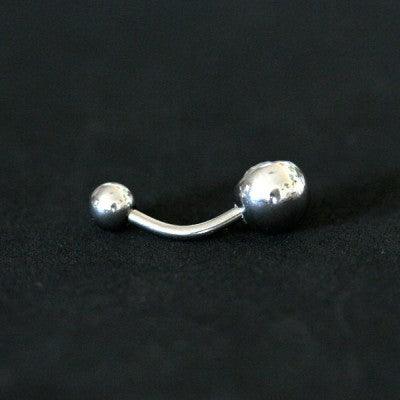 Piercing de umbigo da Tal da Realeza visto por trás em um fundo preto aveludado. A peça é feita de aço cirúrgico e conta com uma pedra de cristal  em uma das extremidades.