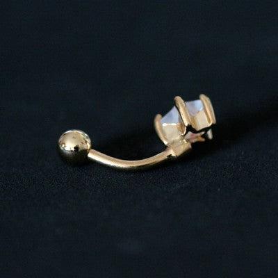 Piercing de umbigo da Tal da Realeza visto por trás em um fundo preto aveludado. A peça é dourada e conta com uma pedra de zircônia.