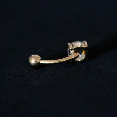 Piercing de umbigo da Tal da Realeza visto por trás em um fundo preto aveludado. A peça possui uma zircônia em uma das extremidades.