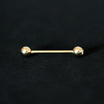 Piercing Barbell da Tal da Realeza em um fundo preto aveludado. A peça é dourada, reta e possui esferas nas extremidades, sendo uma delas com pedra de cristal.