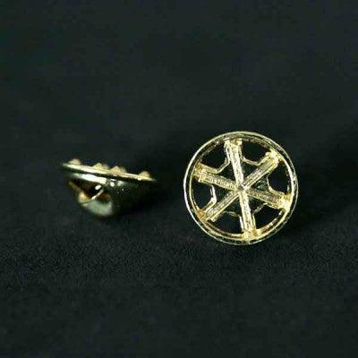 Broche Agronomia folheado a ouro em um fundo preto. A peça tem o formato de uma engrenagem.