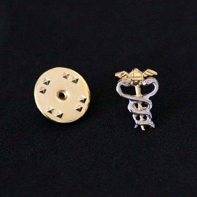 Broche Contabilidade folheado a ouro em um fundo preto. A peça tem formato de um elmo alado com duas serpentes entrelaçadas.