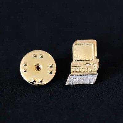 Broche Computação folheado a ouro em um fundo preto. A peça tem formato de um computador antigo.