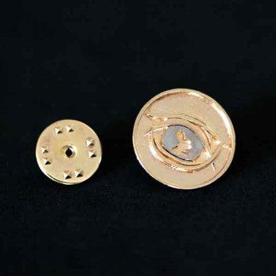 Broche Oftalmologia folheado a ouro em um fundo preto. A peça tem formato circular, com um olho em relevo ao centro.