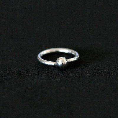 Piercing Captive Esfera da Tal da Realeza em um fundo preto aveludado. A peça é prateada, tem formato circular e possui um detalhe em formato esférico.