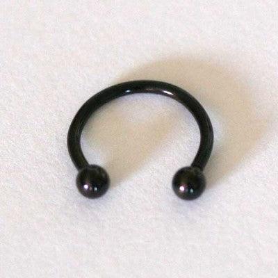 Piercing Barbell da Tal da Realeza em um fundo branco aveludado. A peça é preta, tem formato de ferradura e possui esferas nas extremidades.