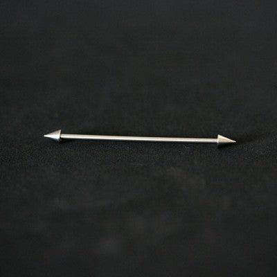 piercing transversal em aço cirúrgico da tal da realeza em um fundo preto aveludado. a peça possui formato de spikes em suas extremidades.
