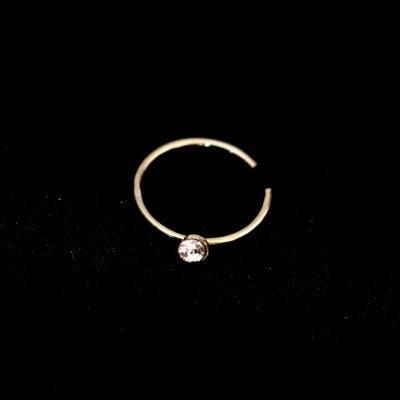 Piercing Nostril Argola em aço cirúrgico da Tal da Realeza em um fundo preto aveludado. A peça também possui uma pedra brilhante.