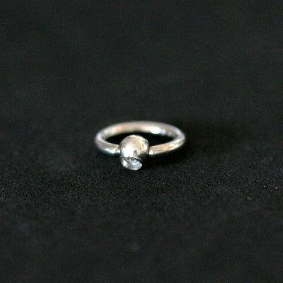 Piercing Captive Esfera da Tal da Realeza em um fundo branco aveludado. A peça é prateada, tem formato circular e possui um detalhe esférico com pedra de cristal.