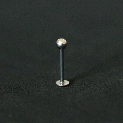 piercing labret da tal da realeza em um fundo preto aveludado. a peça é prateada e possui uma esfera com na extremidade.
