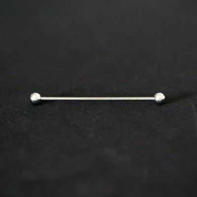 Piercing Transversal em aço cirúrgico da Tal da Realeza em um fundo preto aveludado. A peça possui formato de esferas em suas extremidades.