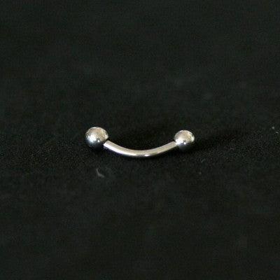 Piercing de aço cirúrgico com haste curva e esferas nas extremidades sobre fundo preto. Uma das esferas possui uma pedra de cristal.