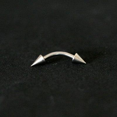 Piercing de aço cirúrgico com haste curva e spikes nas extremidades sobre fundo pretof