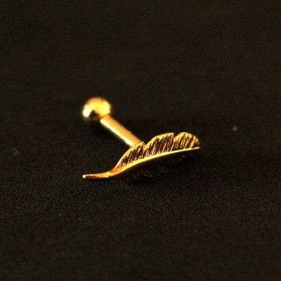 Piercing Tragus folheado a ouro da Tal da Realeza visto pela diagonal em um fundo preto aveluadado. A peça tem formato de pena em uma das pontas.