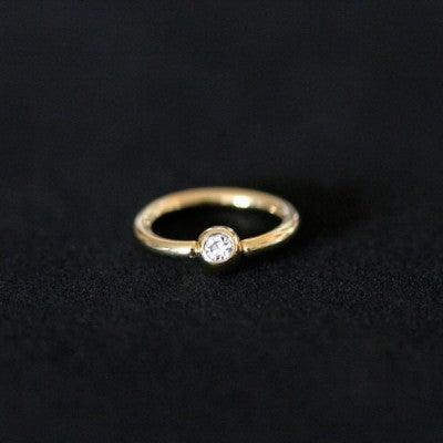 Piercing Captive Esfera da Tal da Realeza em um fundo branco aveludado. A peça é dourada, tem formato circular e possui um detalhe esférico com pedra de cristal.