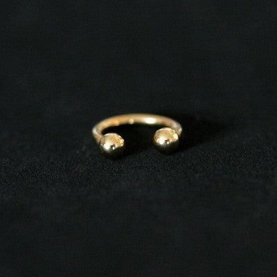 Piercing Barbell da Tal da Realeza em um fundo preto aveludado. A peça é dourada, tem formato de ferradura e possui esferas nas extremidades.