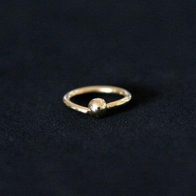Piercing Captive Esfera da Tal da Realeza em um fundo branco aveludado. A peça é dourada, tem formato circular e possui um detalhe em formato esférico.