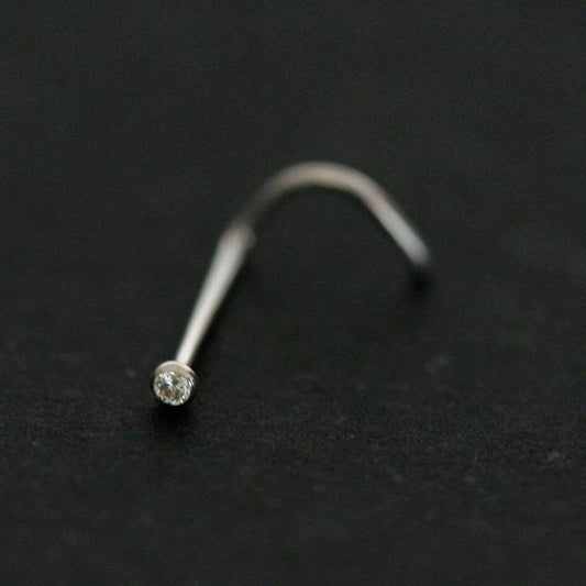 Piercing Nostril em Ouro Branco da Tal da Realeza em um fundo preto. A peça possui uma pedra de brilhante na ponta.