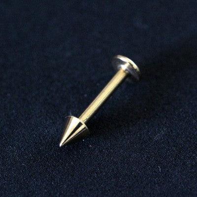 Piercing labret da Tal da Realeza em um fundo preto aveludado. A peça é dourada e possui spike na extremidade.