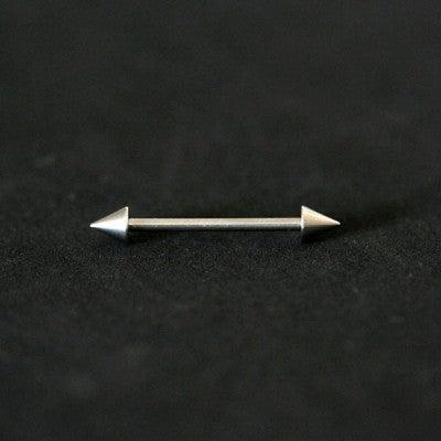 Piercing de aço cirúrgico com formato de barra reta com spikes nas extremidades sobre fundo preto.