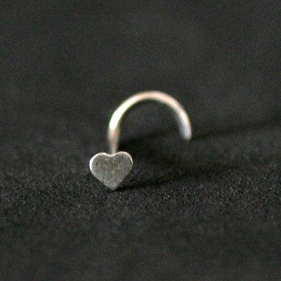 Piercing Nostril em aço cirúrgico da Tal da Realeza em um fundo preto aveludado. A peça tem formato de coração na ponta.