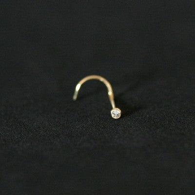 piercing nostril folheado a ouro da tal da realeza em um fundo preto aveludado. a peça tem uma pedra de cristal na ponta.