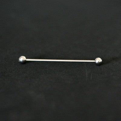 piercing transversal em aço cirúrgico da tal da realeza em um fundo preto aveludado. a peça possui pedras de cristal em suas extremidades.