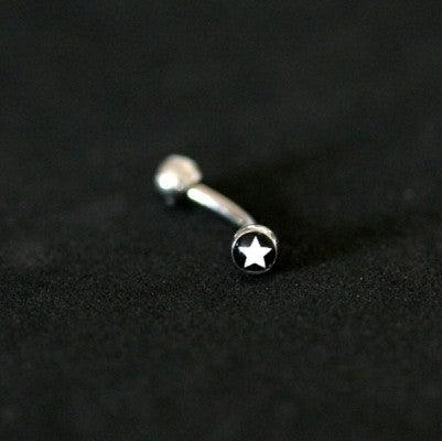 Piercing de aço cirúrgico com haste curva e esferas nas extremidades sobre fundo preto. As esferas possuem estampas de estrela.