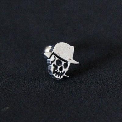 Piercing Tragus em aço cirúrgico da Tal da Realeza em um fundo preto aveludado. A peça tem formato de caveira em uma das extremidades.