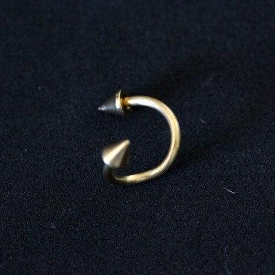 Piercing Twister da Tal da Realeza em um fundo preto aveludado. A peça é dourada, tem um formato espiralado e conta com spikes nas extremidades.