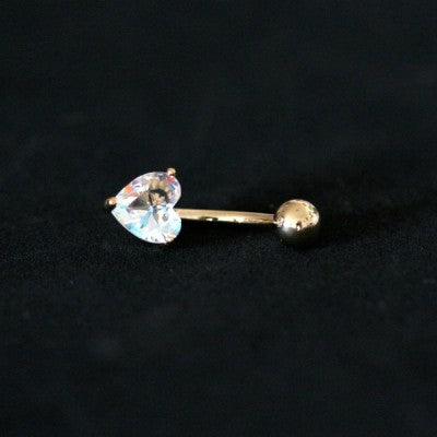 Piercing de umbigo da Tal da Realeza visto de frente em um fundo preto aveludado. A peça é dourada e conta com uma pedra de zircônia em formato de coração.