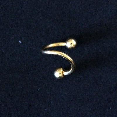 Piercing Twister da Tal da Realeza em um fundo preto aveludado. A peça é dourada, tem um formato espiralado e conta com esferas nas extremidades.