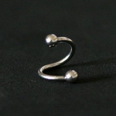 Piercing Twister da Tal da Realeza em um fundo preto aveludado. A peça é prateada, tem um formato espiralado e conta com esferas nas extremidades.