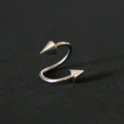 Piercing Twister da Tal da Realeza em um fundo preto aveludado. A peça é prateada, tem um formato espiralado e conta com spikes nas extremidades.